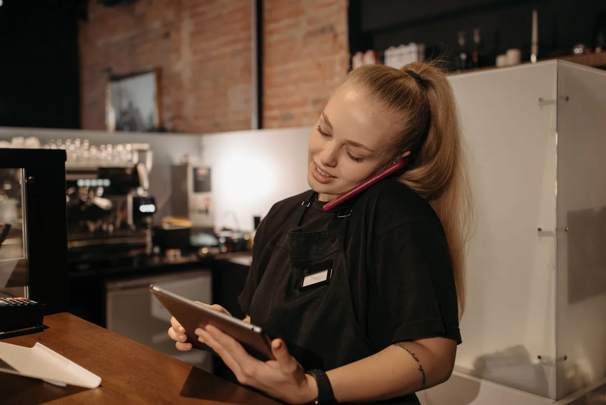 Encargada de una cafetería hablando por teléfono mientras mira la tableta