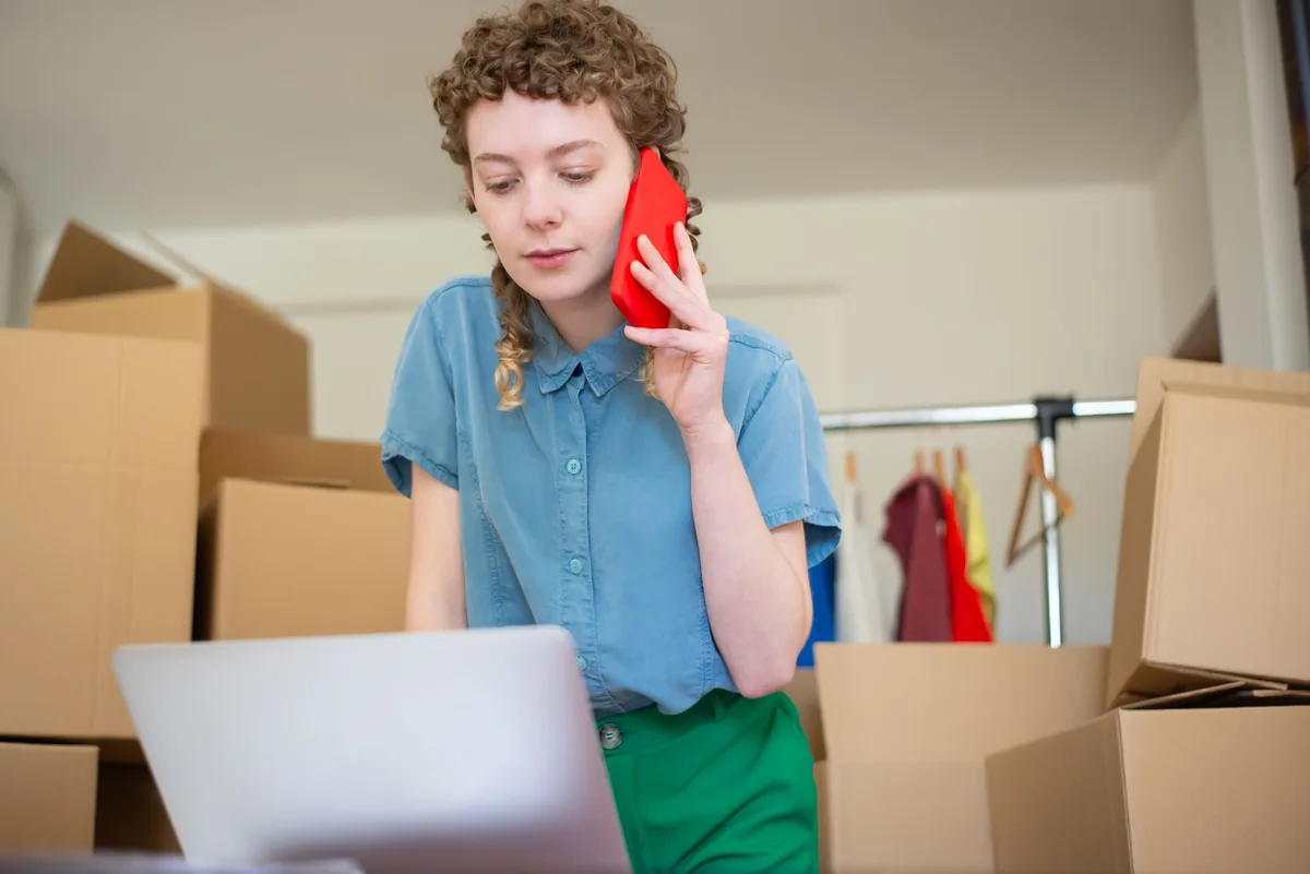 Mujer hablando por teléfono con el portátil abierto entre cajas de mudanza